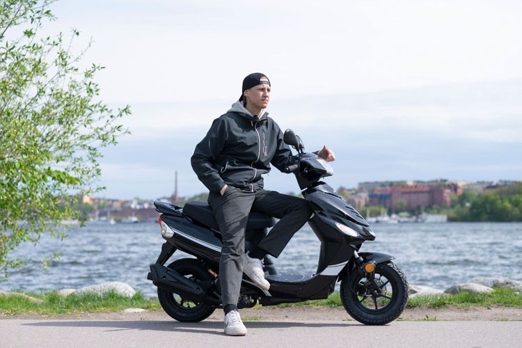 Ung man kör på bakhjulet på sin moped framför ett cafe